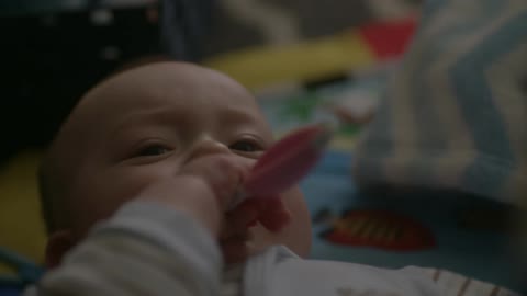 Baby chews on a plastic toy and waves its arms