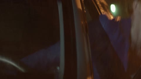 A woman gets out of her vehicle on a rainy night