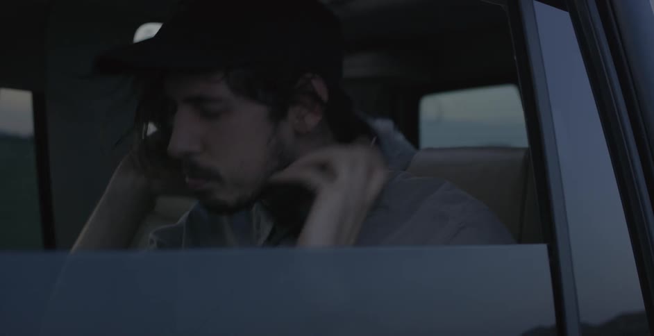 Man sitting in a vehicle rubs his hands with his face and puts on headphones