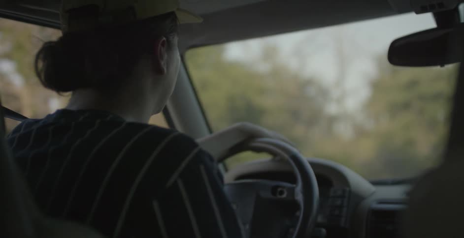 A man drives a car with trees lining the road outside