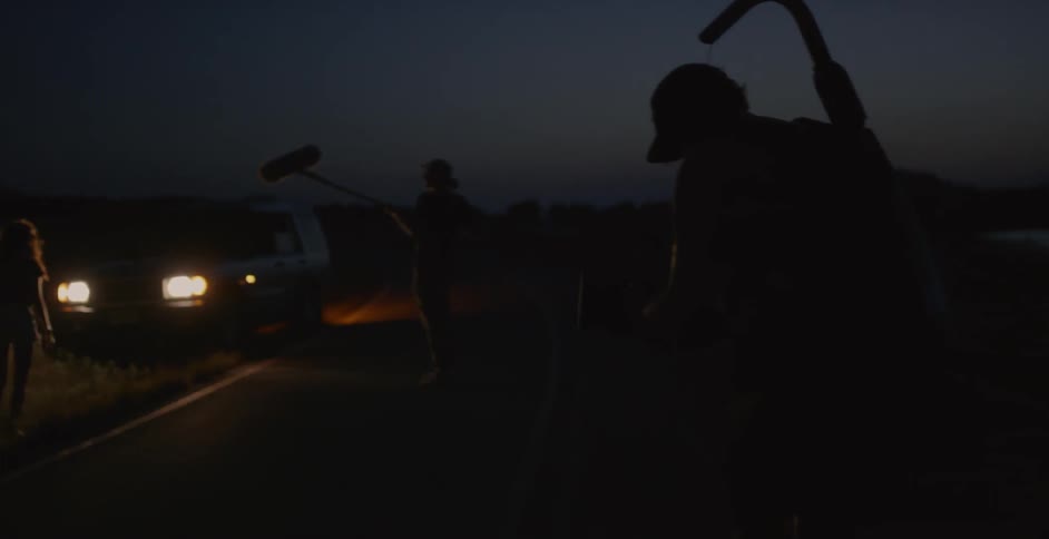 A film crew is shooting a scene by the side of the road at night
