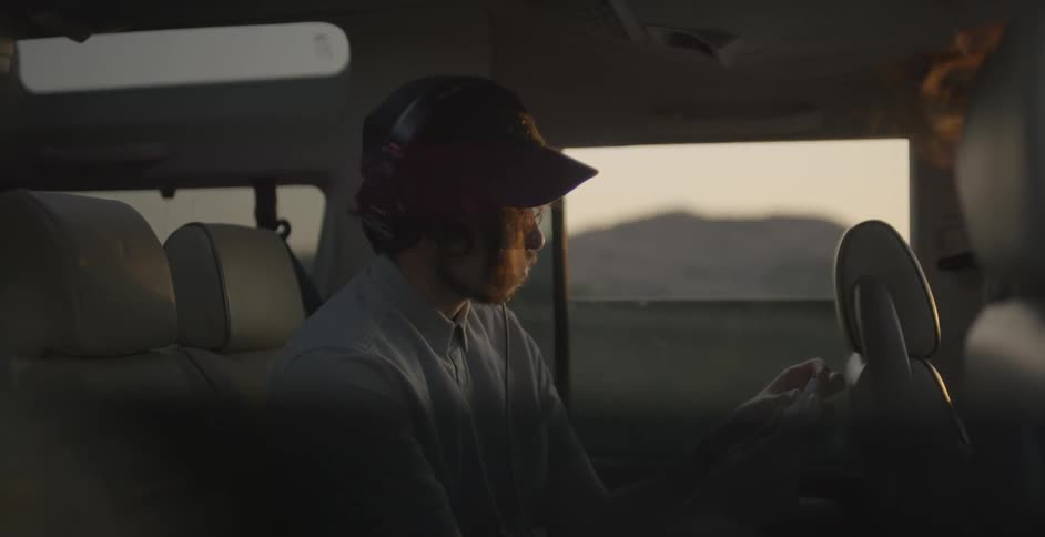 A man rides in a car while wearing headphones and looking at flashcards