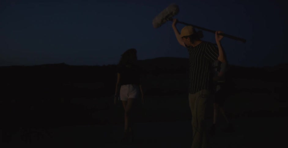 A man is holding a sound mic over a woman at night