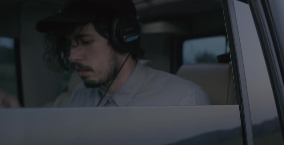 A man placing headphones on his ears as he is in the backseat of a car