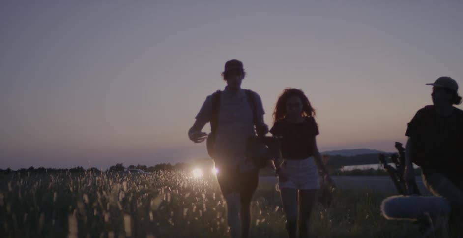 Three people walk together on a field at dawn