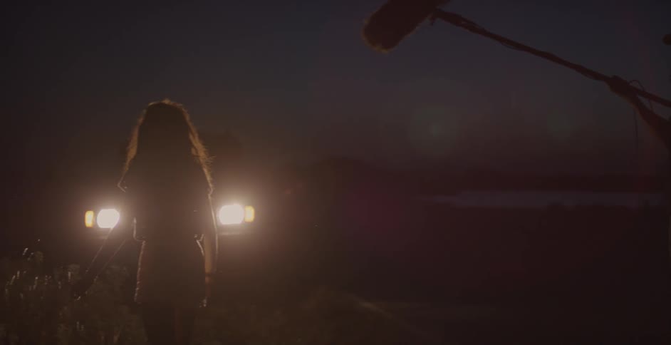A woman is standing in front of a car's headlights at night