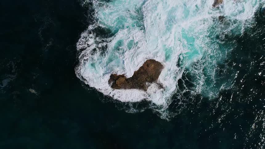 An overhead view of some water crashing over large rocks
