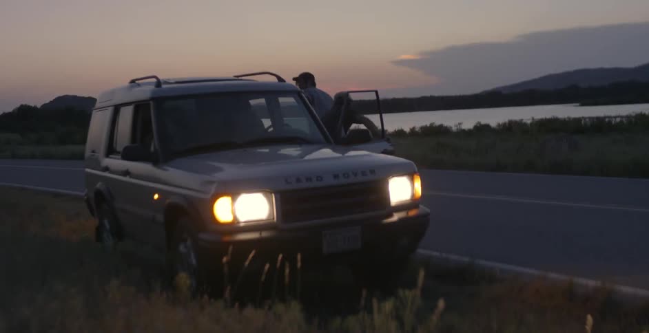A car sitting alongside the road with people rushing to get into it