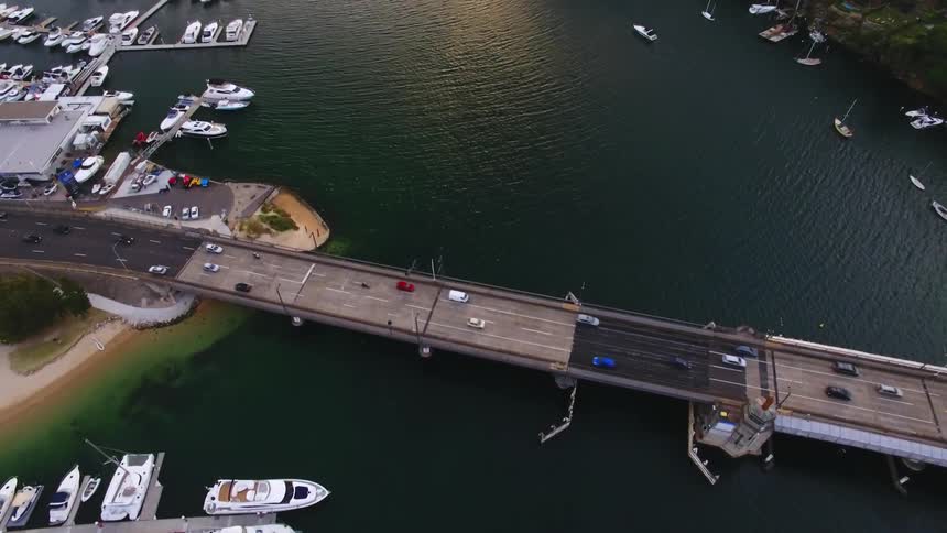 Aerial view of boats parked in a harbor and cars driving over a bridge