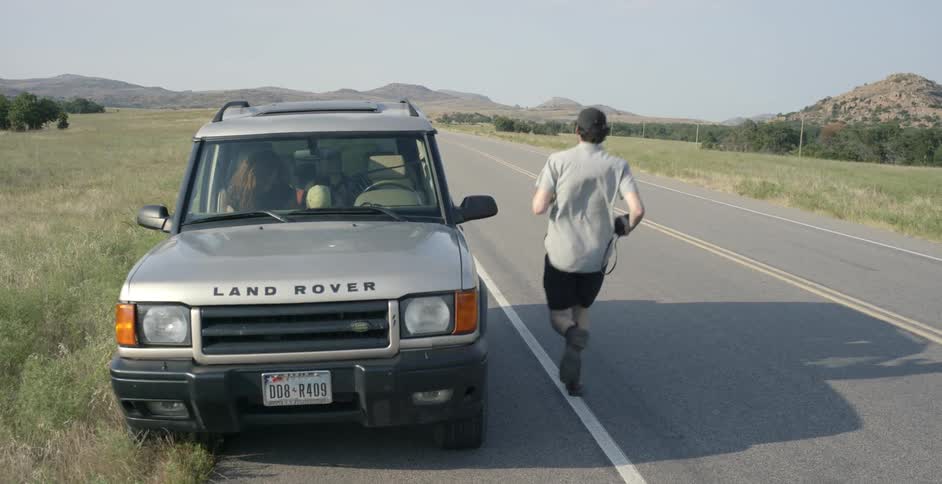 A land rover is parked on the side of a road while a man climbs into a passenger seat