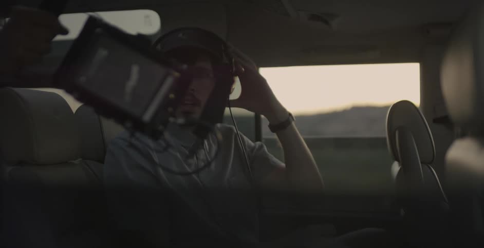 Man sitting in a vehicle puts headphones on and looks at a camera