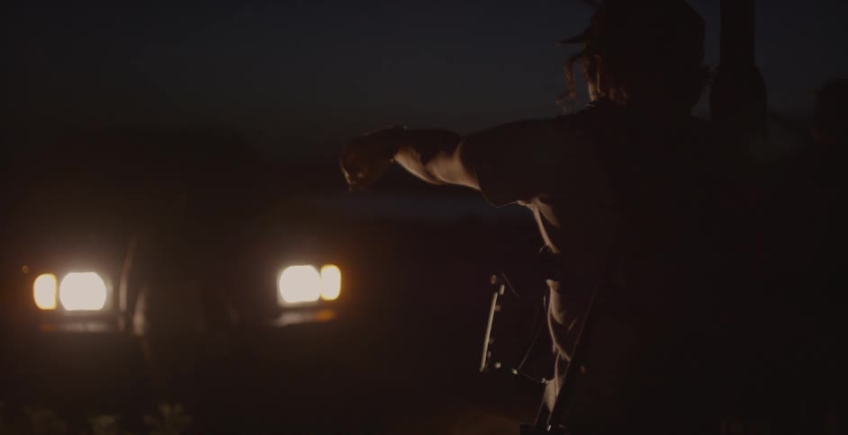 People holding recording equipment illuminated by headlights at night