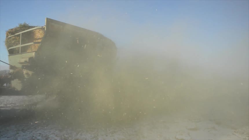 A tractor hauls hay across a snowy field and churns up dust