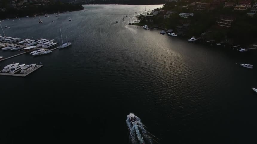Aerial view of boat traveling down a river next to a harbor