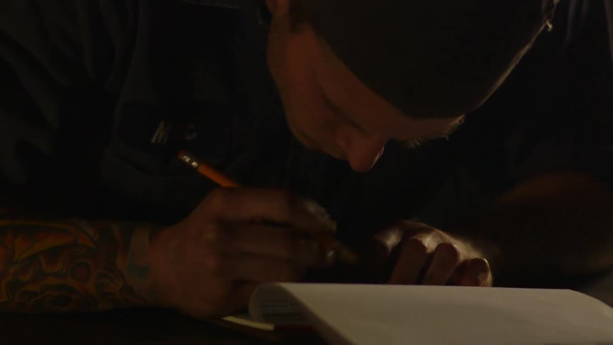 A man writes in a notebook with a pencil