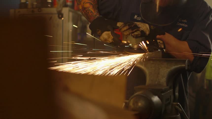 A man is using a tool to grind metal on an anvil