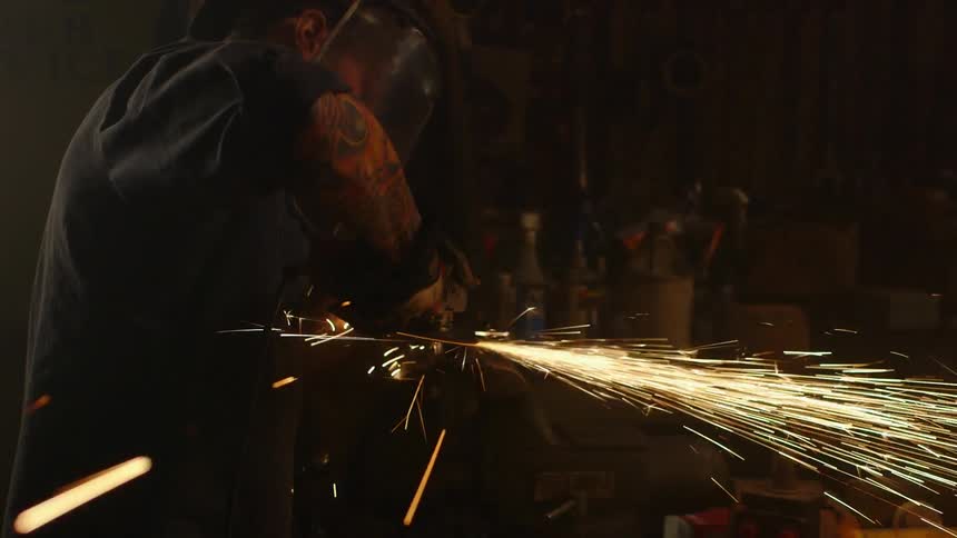 A man uses a power tool that shoots out sparks in a workshop