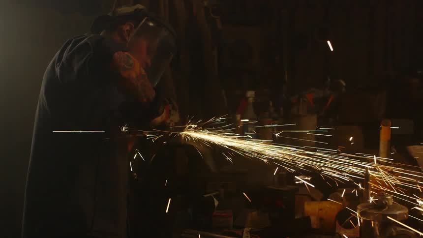 A man is using a tool to grind something in a dark shop