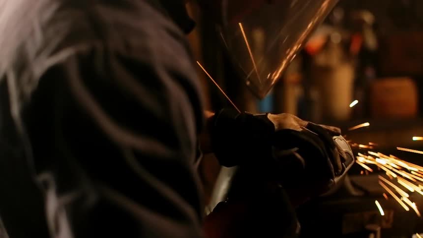 A man wearing a welding mask is grinding metal