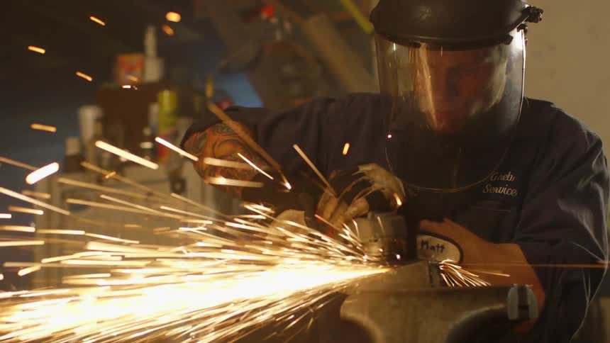 Man grinds a piece of metal with a sander