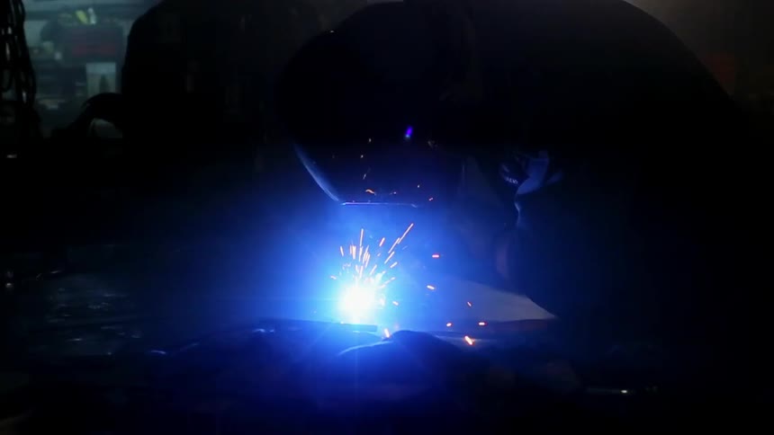 Sparks fly around a welder in a dark room