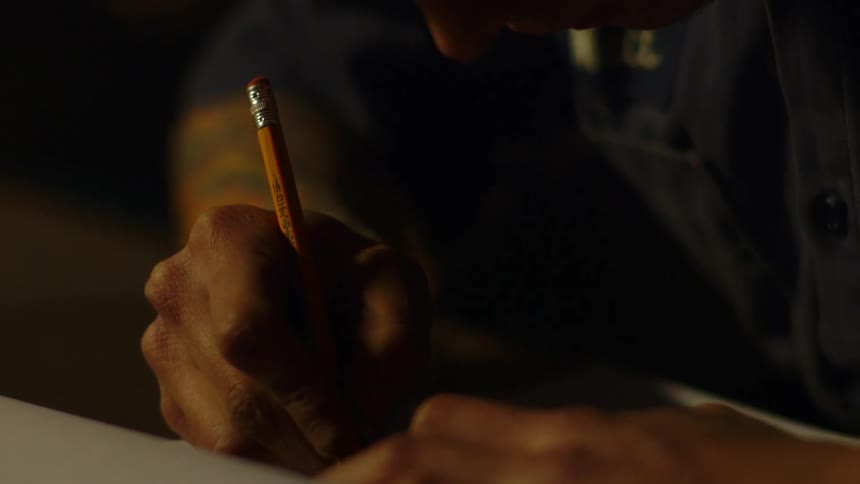 Person writes on a piece of paper with a pencil