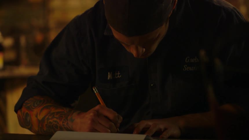 A man with a tattooed arm draws in a notebook
