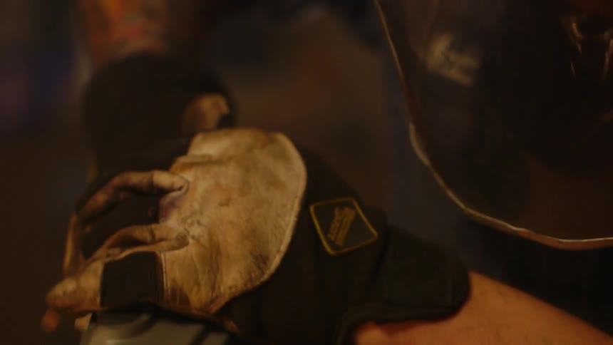 A worker wears a mask while using a grinding power tool as sparks fly all around