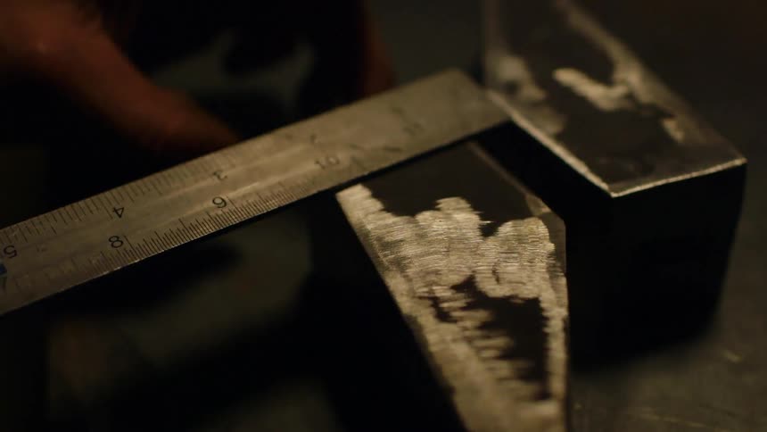 Person measuring a piece of metal with a small ruler