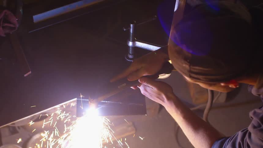 A man is welding a piece of metal held down by a clamp