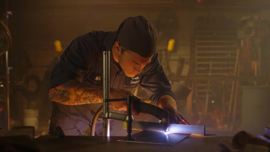 A man leans forward carefully torching pieces of metal together
