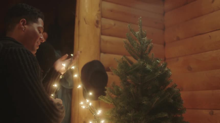 A man and a woman wrapping lights around a christmas tree