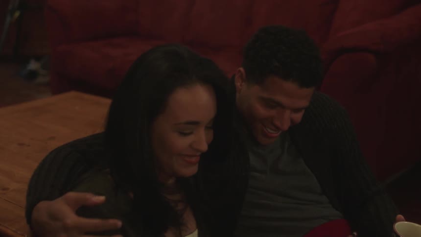 A man puts his arm around a woman as they sit indoors