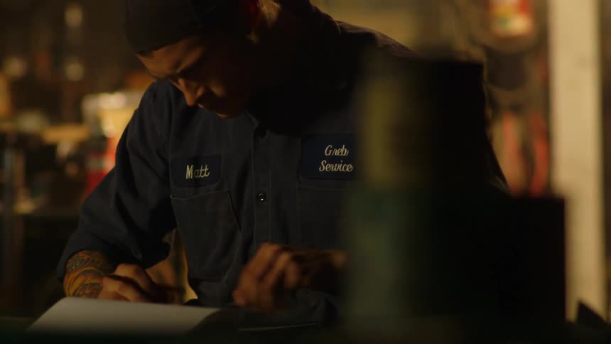 A man sits at a desk in a garage drawing on a pad of paper