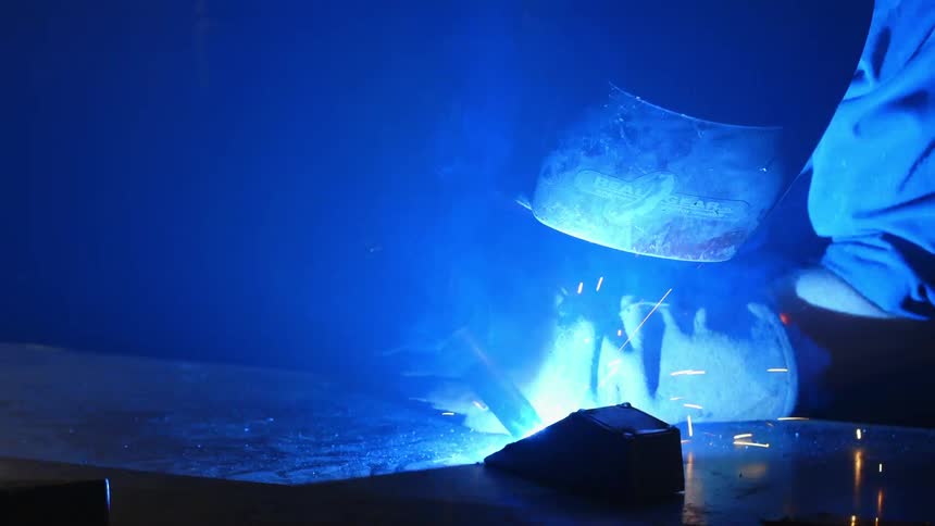A person welds while wearing a welding mask