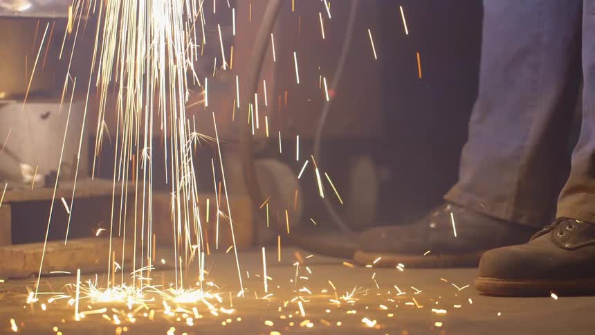 Sparks fly to the floor of a workshop with a man's feet standing nearby