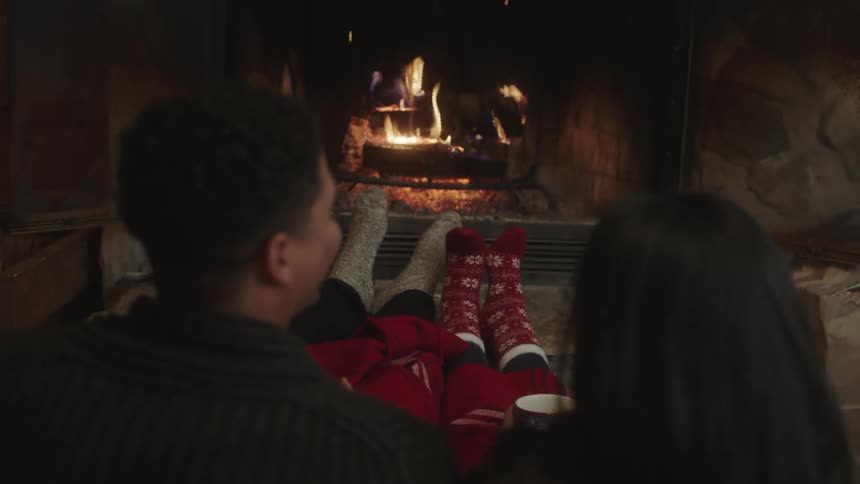 A man and a woman sitting on a couch watching a fire and talking