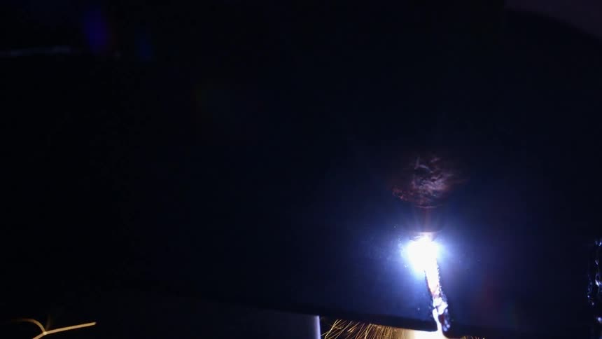 A welder cuts through a piece of metal as sparks fly around