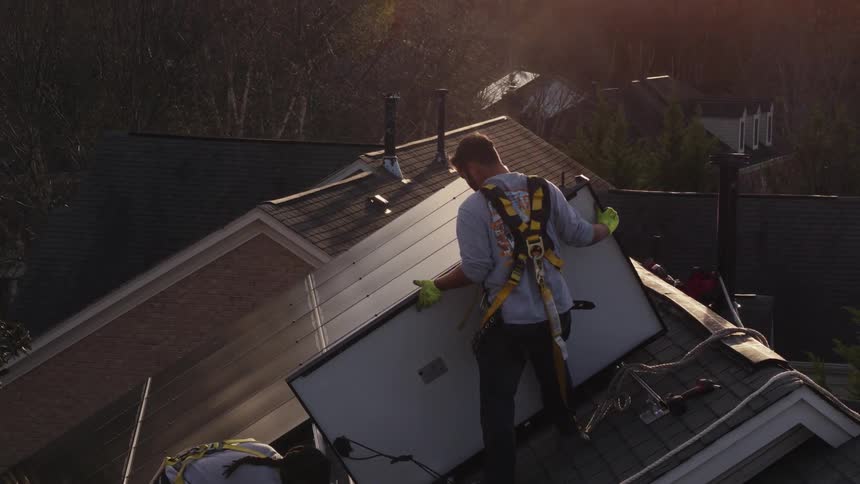Two workers are installing solar panels on a house