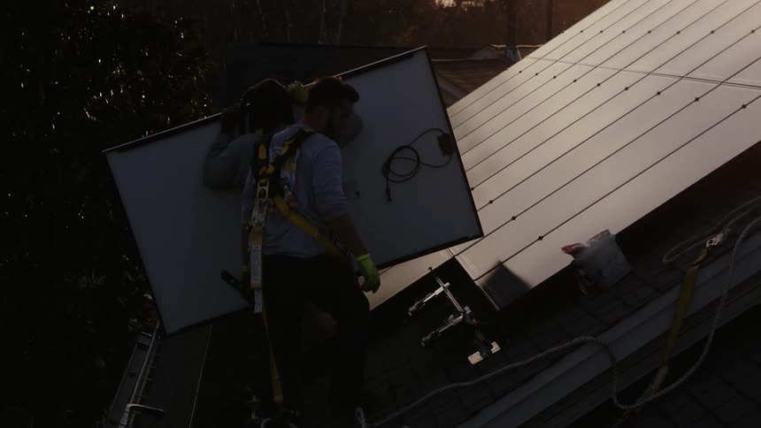 People putting solar panels on a roof at sunset
