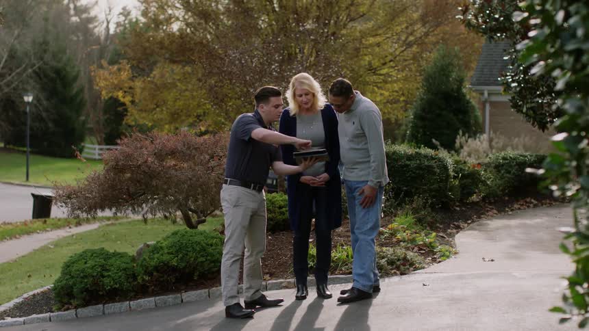 A man shows a couple his tablet in the driveway