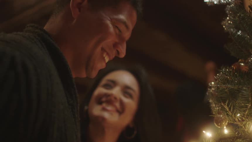 A man and woman smile as they look at their christmas tree