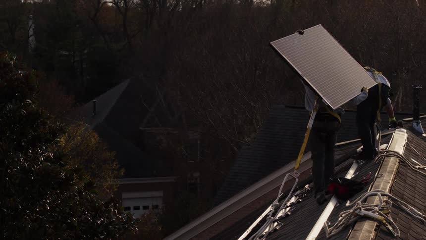Two men work to put solar panels on a roof