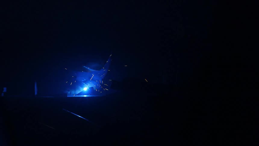 Sparks fly around a welder in a dark room