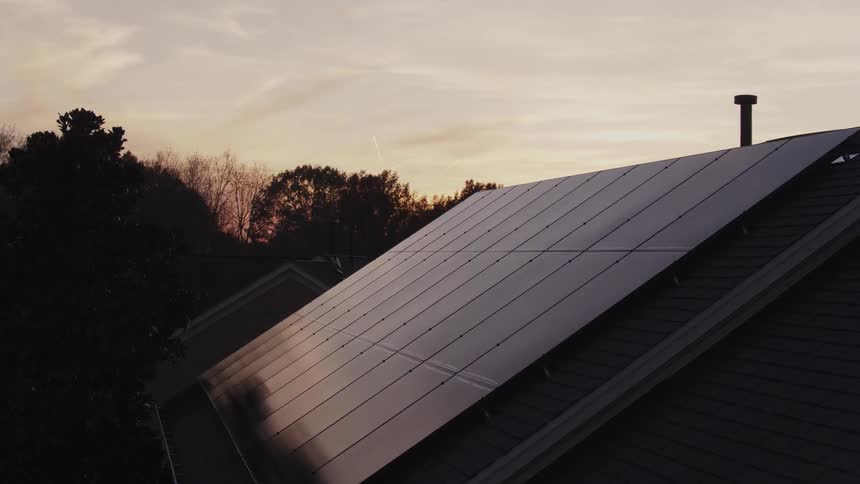 A solar panel covers a house rooftop at sunset