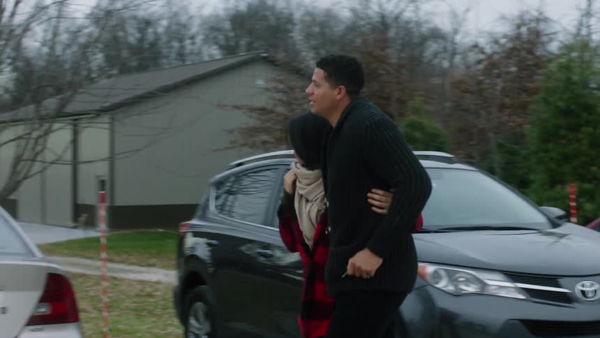 A man and woman are holding each other as they walk in a parking lot
