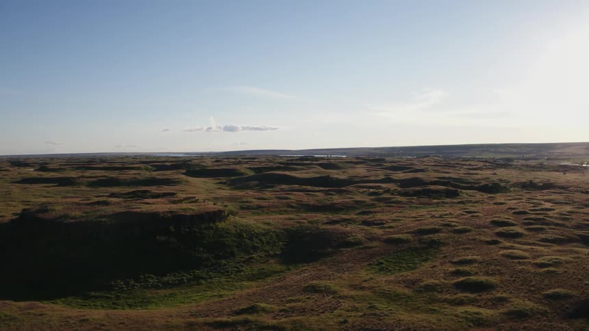 Ascending over a desolate landscape of rough terrain covered with shrubs and sparse grasses