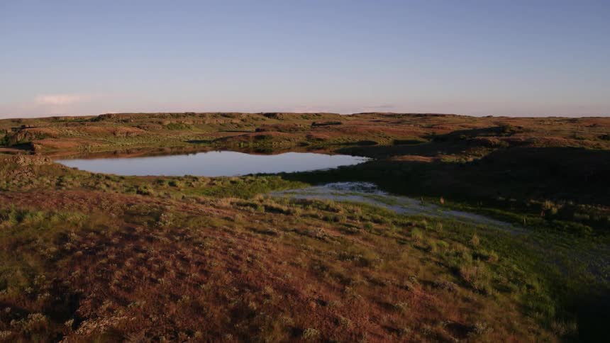 Mirror smooth ponds of water reflect the sky while flying low above rugged scablands