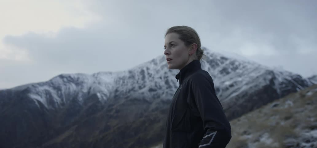A woman stands hands on hips looking at a mountain range