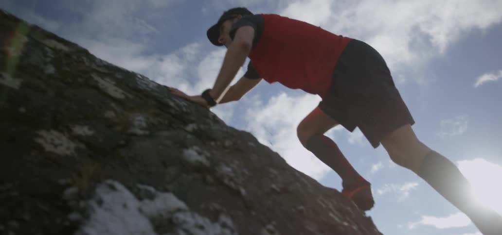 A man climbs a rocky hillside as the sun shines down